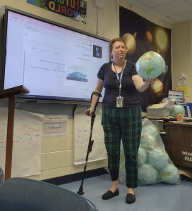 Christine stands in front of her classroom holding a globe